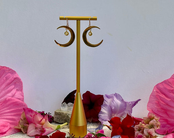Amazing Earth’s Half Moon Earrings with Gold Citrine Dangles on 14KG backs hang on a gold stand, surrounded by colorful flowers and petals, set against a plain white background.