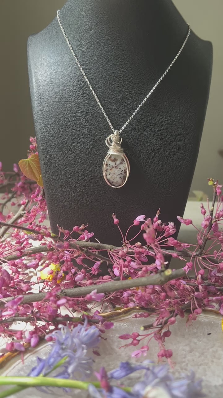 pendant hanging on silver chain on black leather bust. 