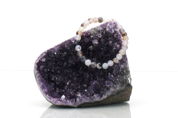 The Amazing Earth Agate Energy Bracelet featuring natural stone beads is draped over a large purple amethyst crystal cluster, set against a white background.