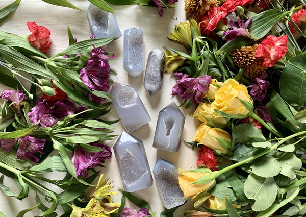 Amazing Earth Agate Towers with Druzy Windows are displayed on a white surface, surrounded by vibrant yellow roses and assorted purple, red, and green flowers and leaves.