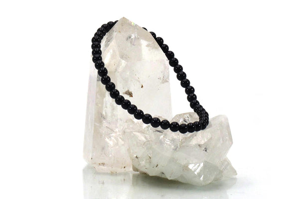 The Amazing Earth Black Tourmaline Energy Bracelet is displayed atop two clear quartz crystals on a white background, making for an eye-catching crystal jewelry piece.